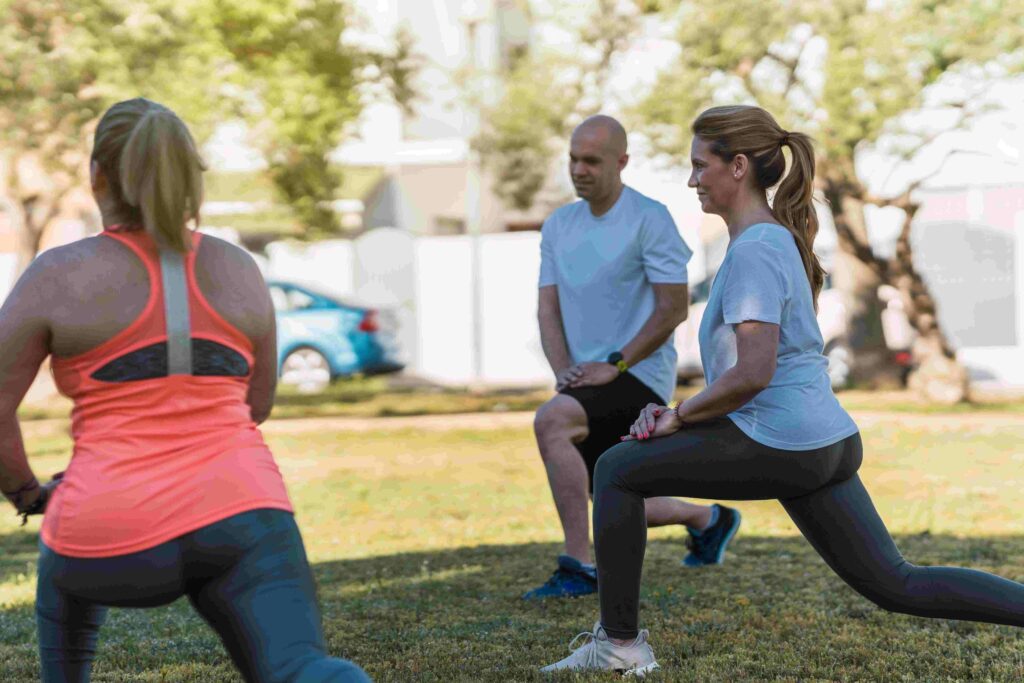 Três pessoas praticando exercícios ao ar livre, realizando afundos para fortalecer pernas e melhorar o condicionamento físico.
