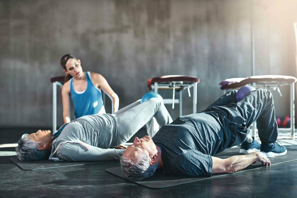 Idosos fazendo exercício de fortalecimento muscular com bola, acompanhados por profissional de educação física.
