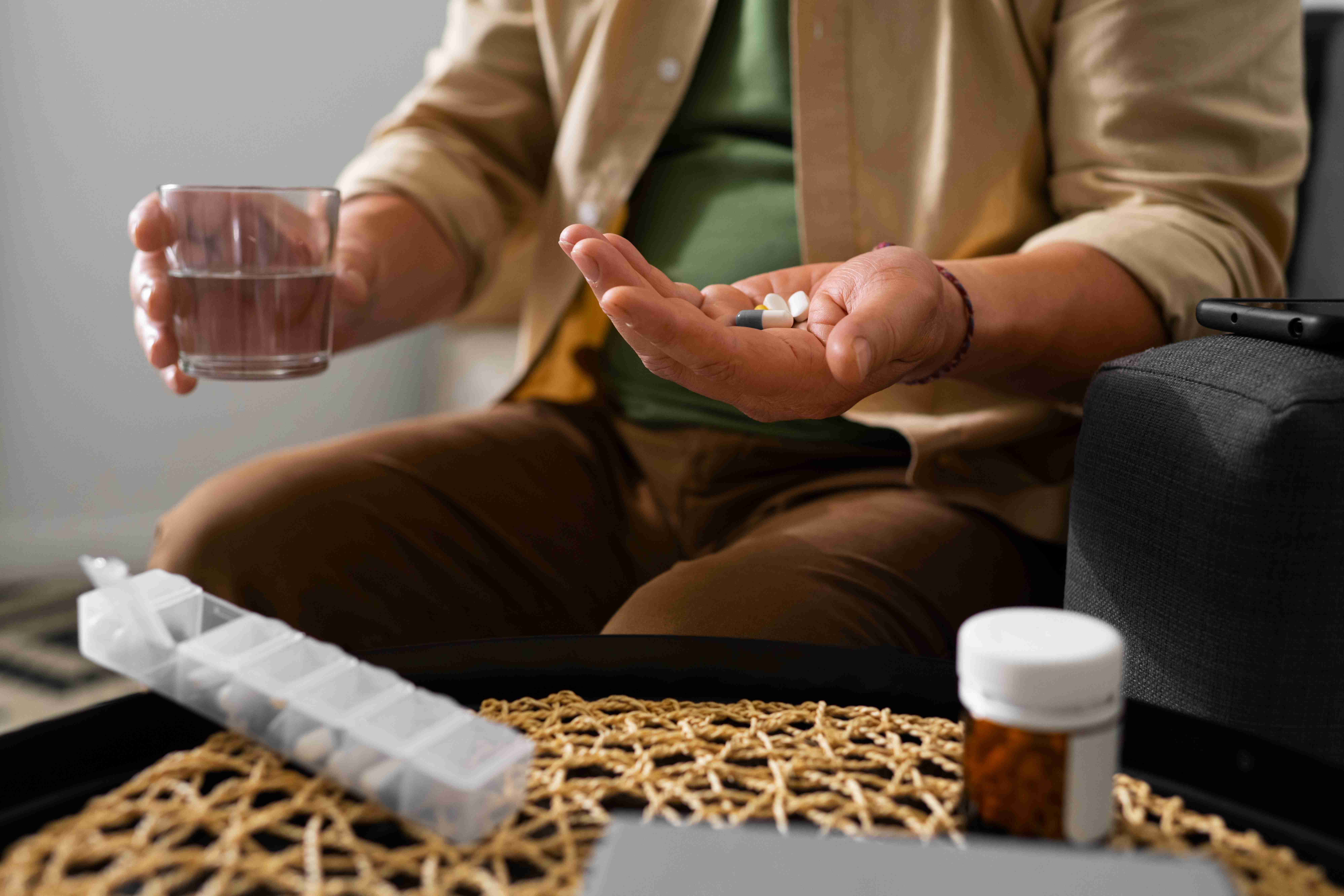 Pessoa com comprimidos na mão e copo d’água, simbolizando o uso de medicamentos para osteoartrite no quadril.